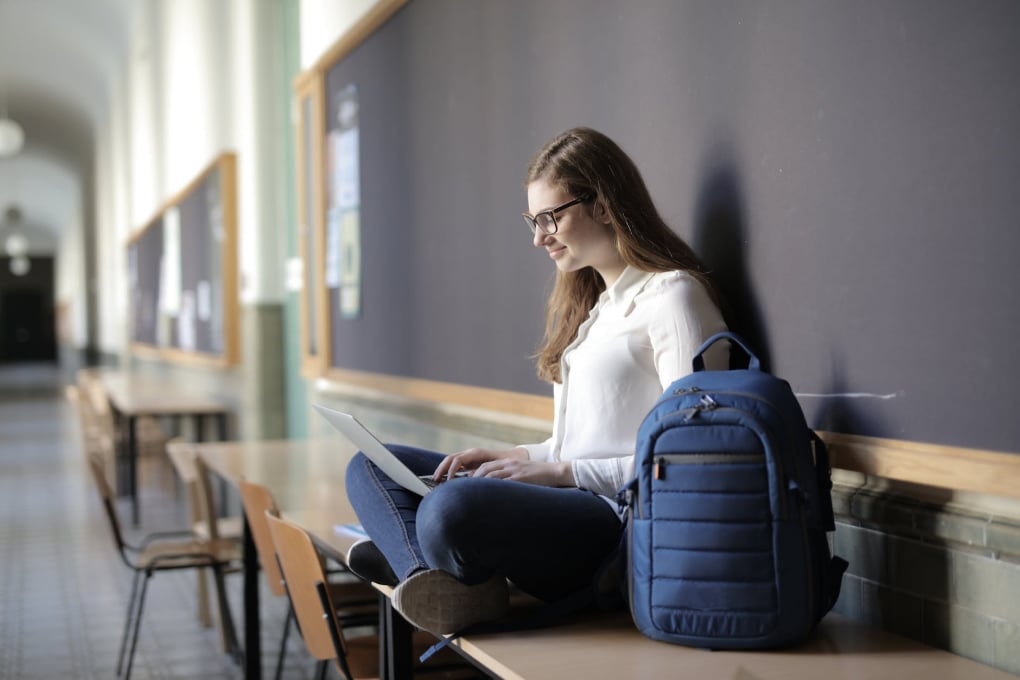 A young professional woman studies alone in a hallway with a laptop and backpack — symbolizing flexible, learner-centered virtual education
